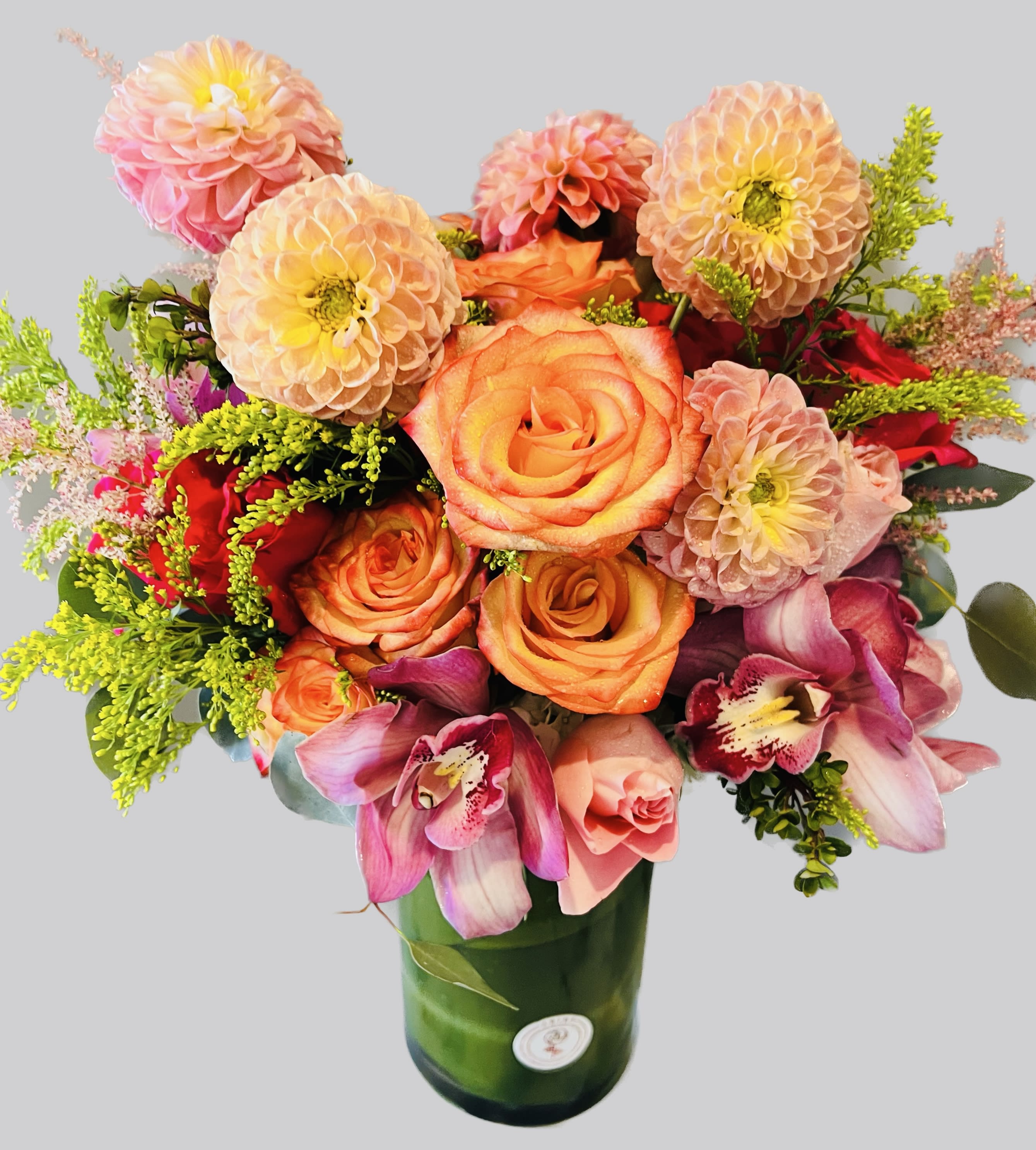 Bouquet of orange roses and pink dahlias in a green glass vase