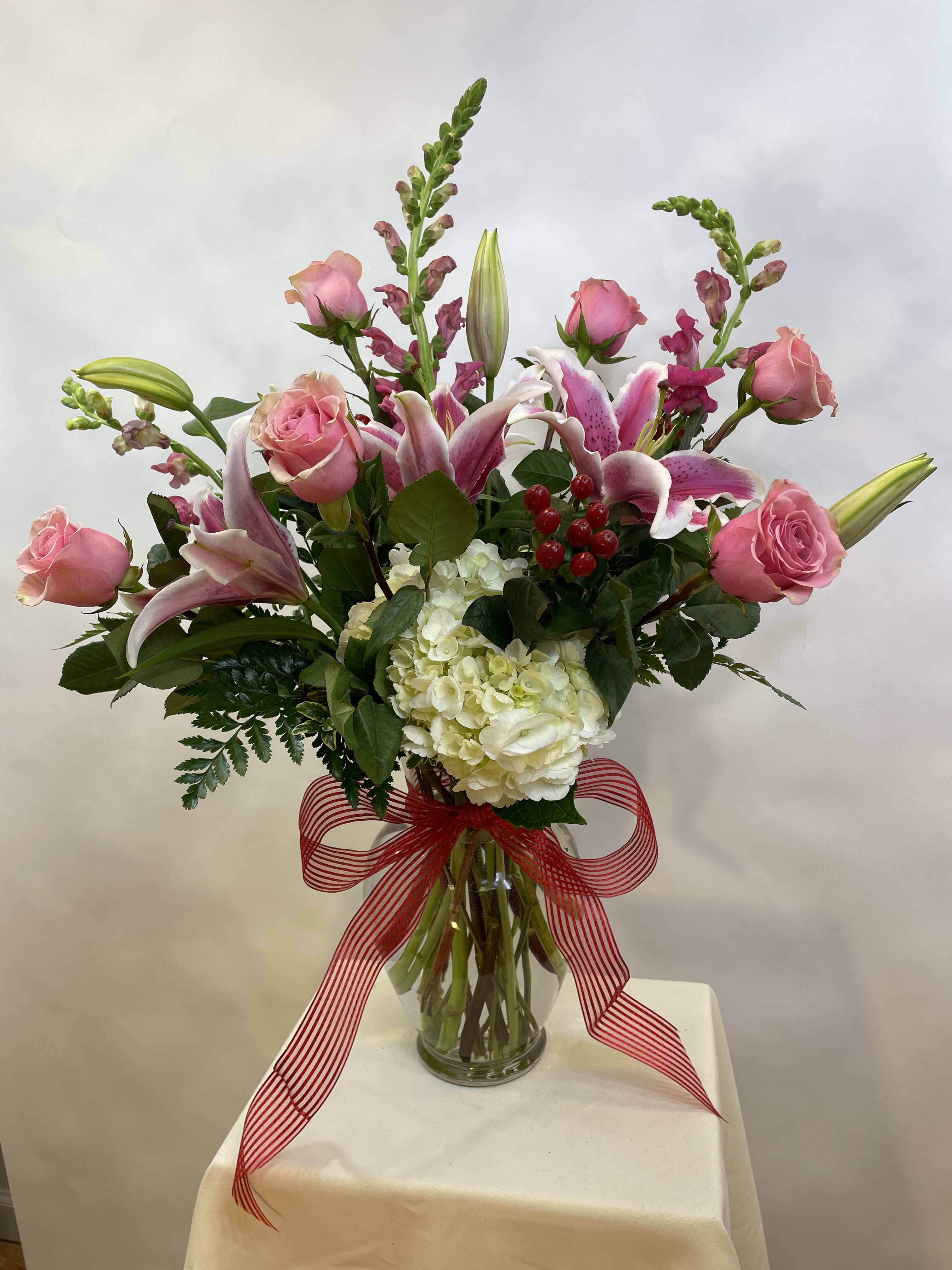Pink roses and lilies arranged in a glass vase with a red striped ribbon.