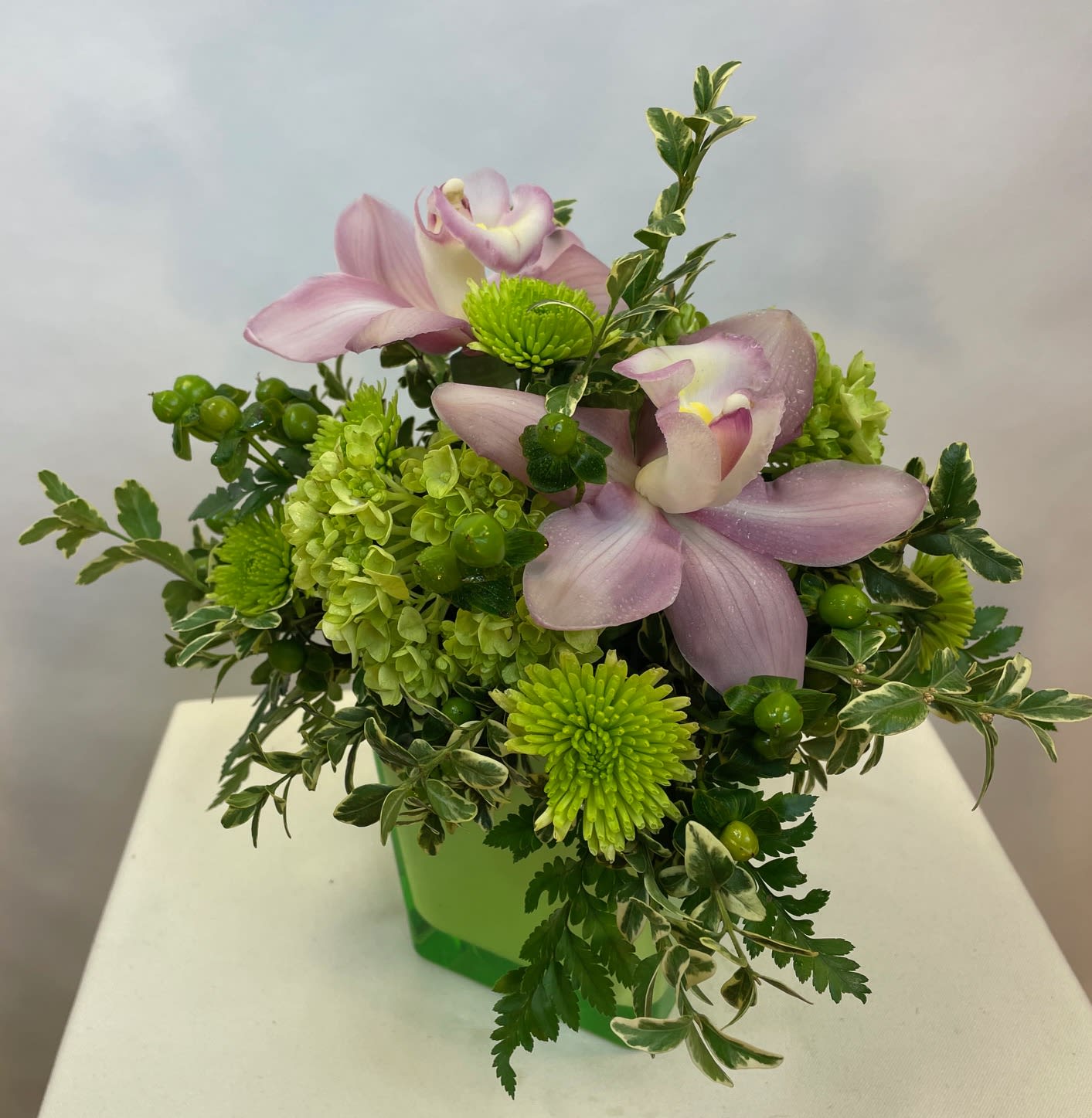 Pink orchids and green mums in a green glass vase