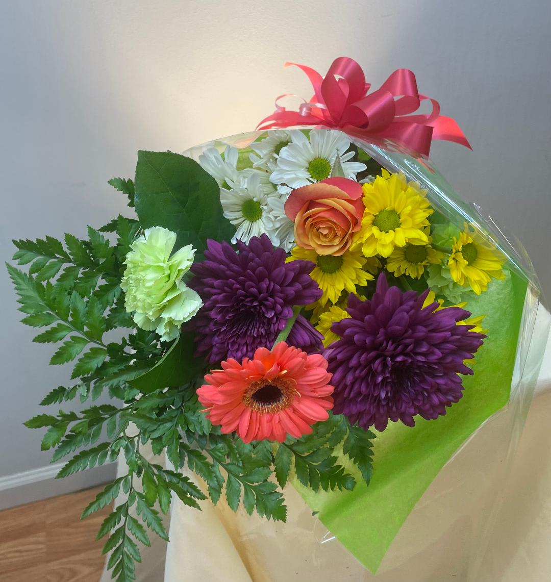 Mixed bouquet with daisies, a rose, gerbera, and chrysanthemums wrapped in clear plastic
