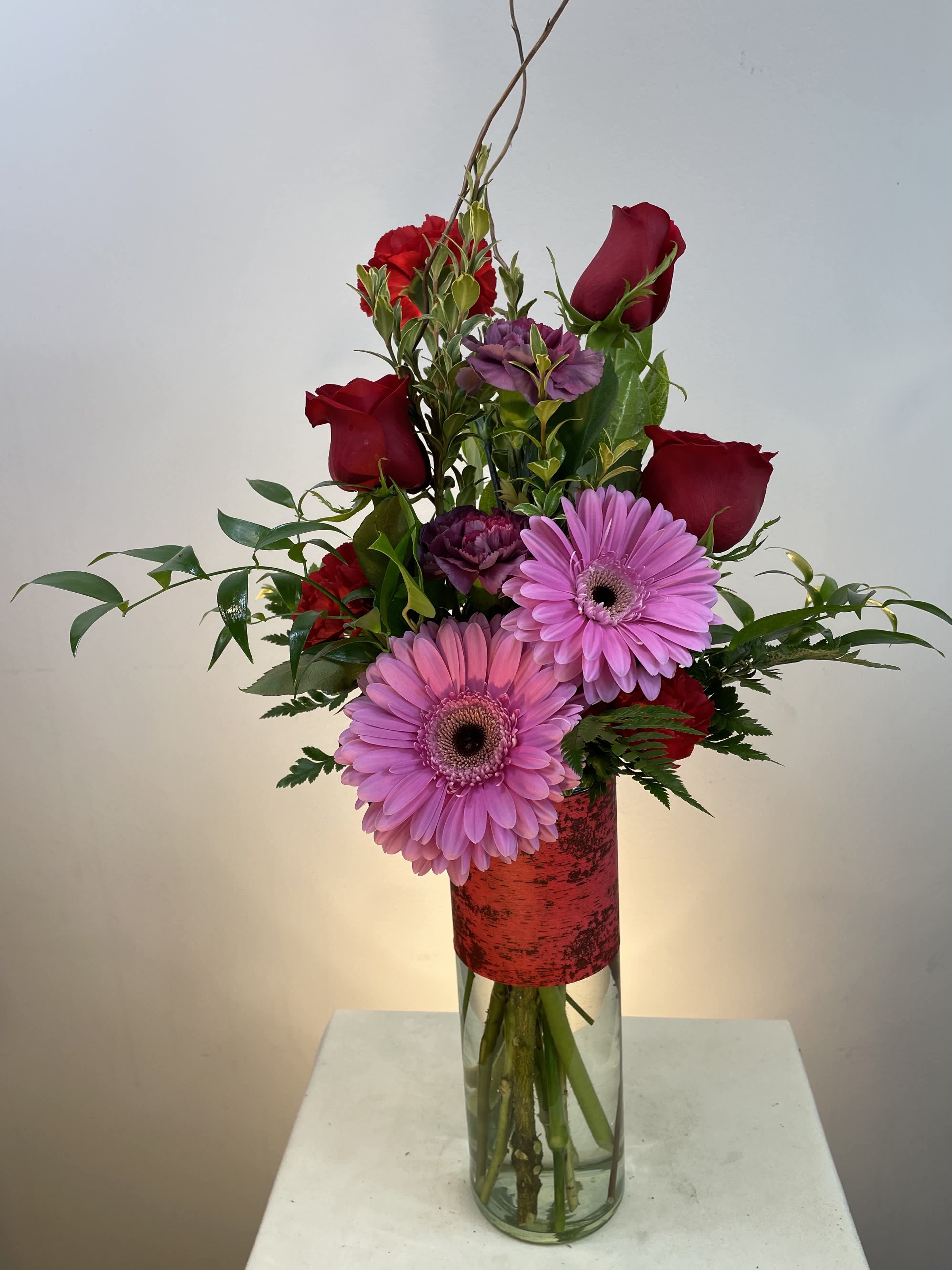 Tall bouquet of red roses and pink gerbera daisies in a glass vase