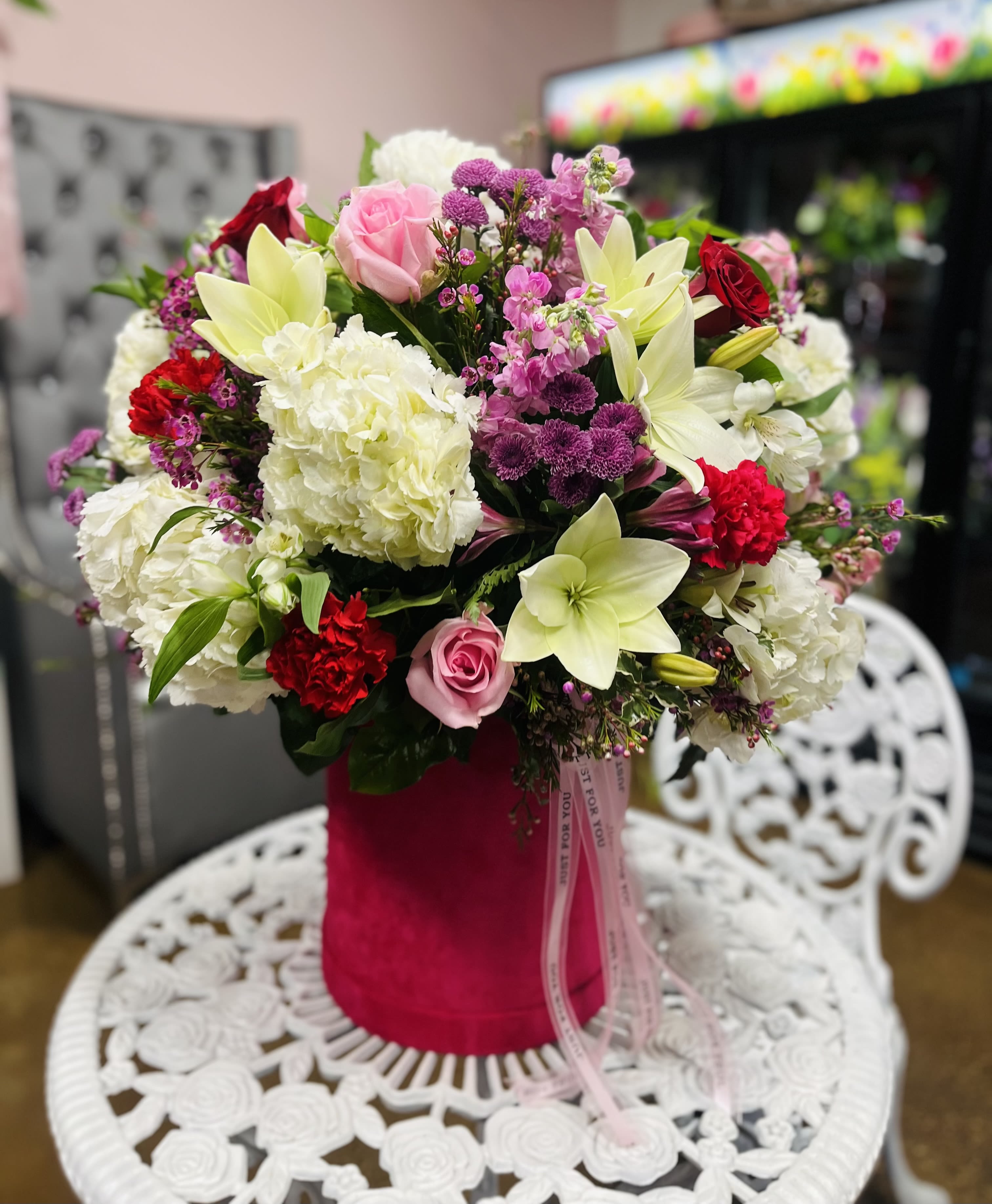 Mixed bouquet of pink roses, white lilies, and red carnations in a pink vase