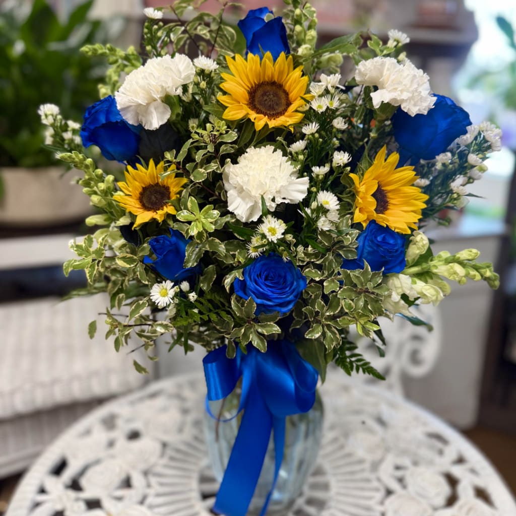 Bouquet of blue roses, sunflowers, and white carnations in a glass vase