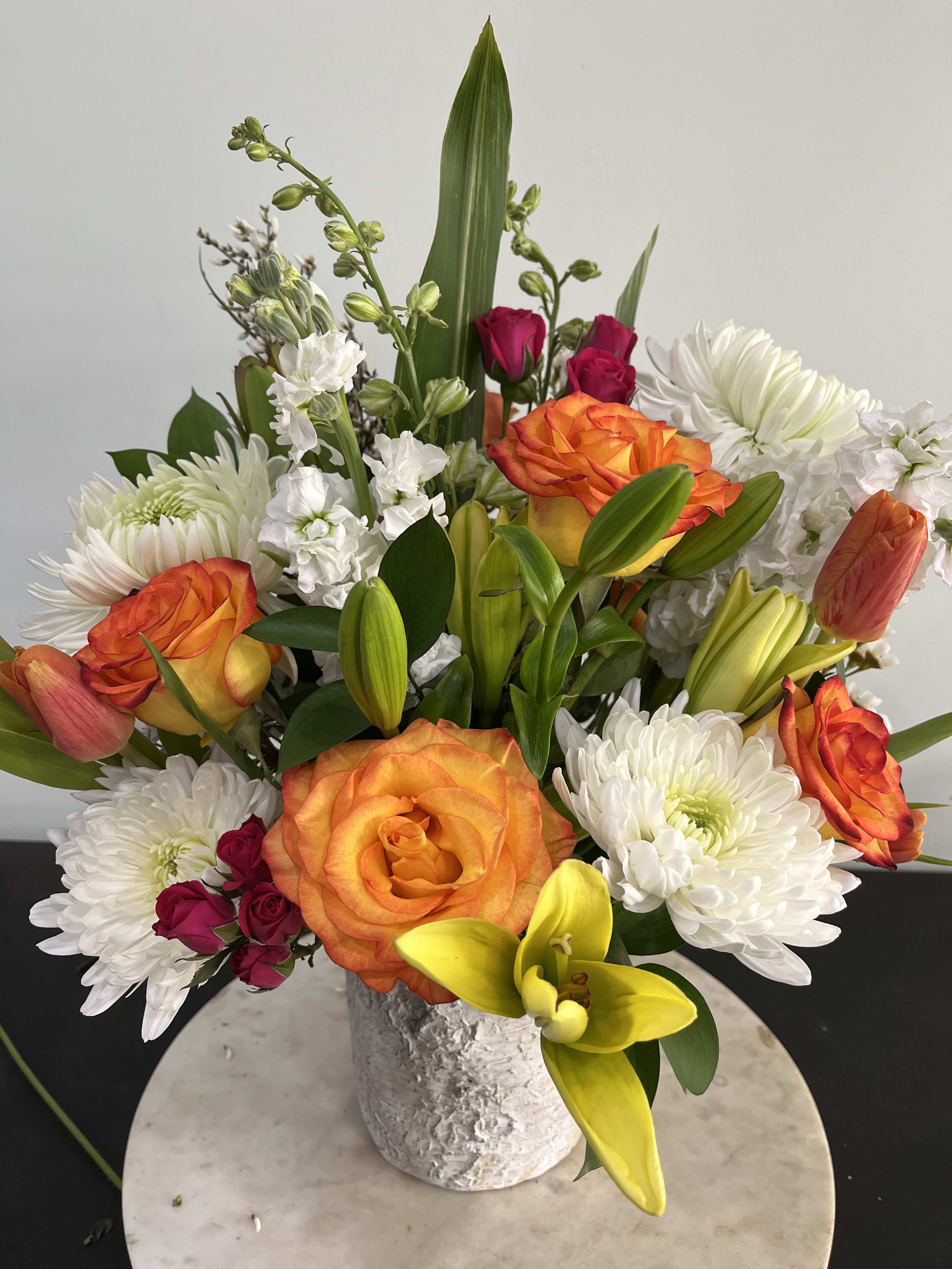 Mixed bouquet of orange roses, white chrysanthemums, and yellow lilies in a textured vase