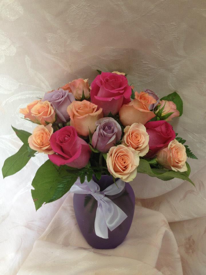 Bouquet of pink, peach, and lavender roses in a purple vase with a ribbon
