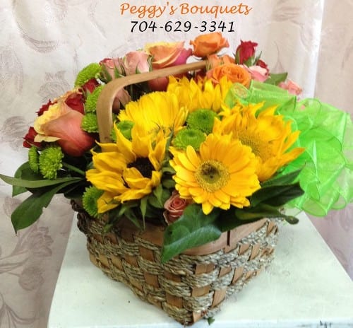 Basket of yellow sunflowers and mixed roses with green tissue wrap