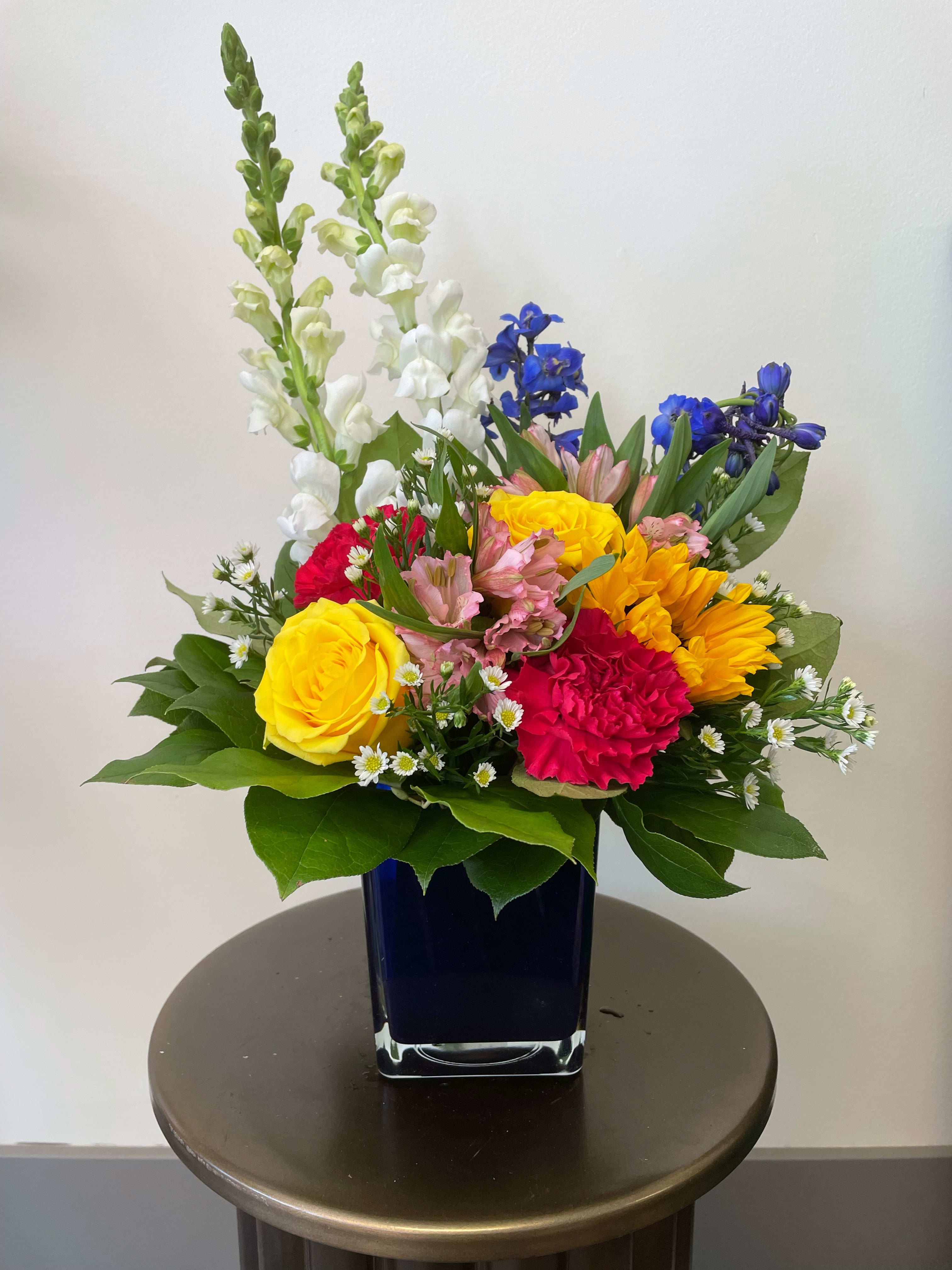 Bright Blessings - *Please specify which vase color you would like in Special Instructions* A multicolored arrangement in a colored cube featuring snapdragons, roses, alstroemerias, and more! This fun arrangement is perfect for any occasion such as birthdays, thank you, or get well. Vase color options are yellow, dark blue, light blue, or orange.