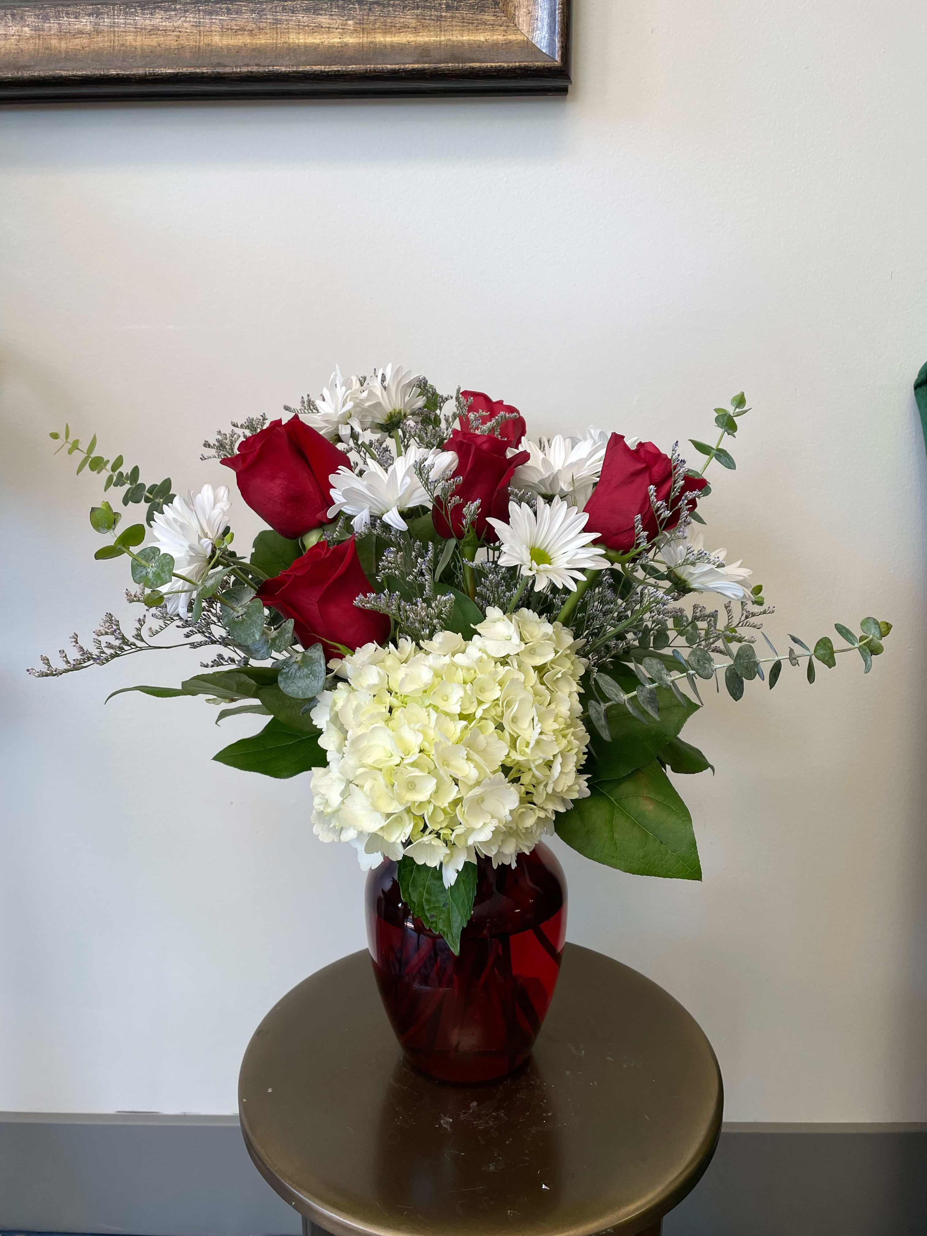 Romantic Type - This romantic one-sided arrangement comes in a red glass vase and features red roses, white daisies, white hydrangea, and purple limonium. Send this to your special someone to earn some brownie points!