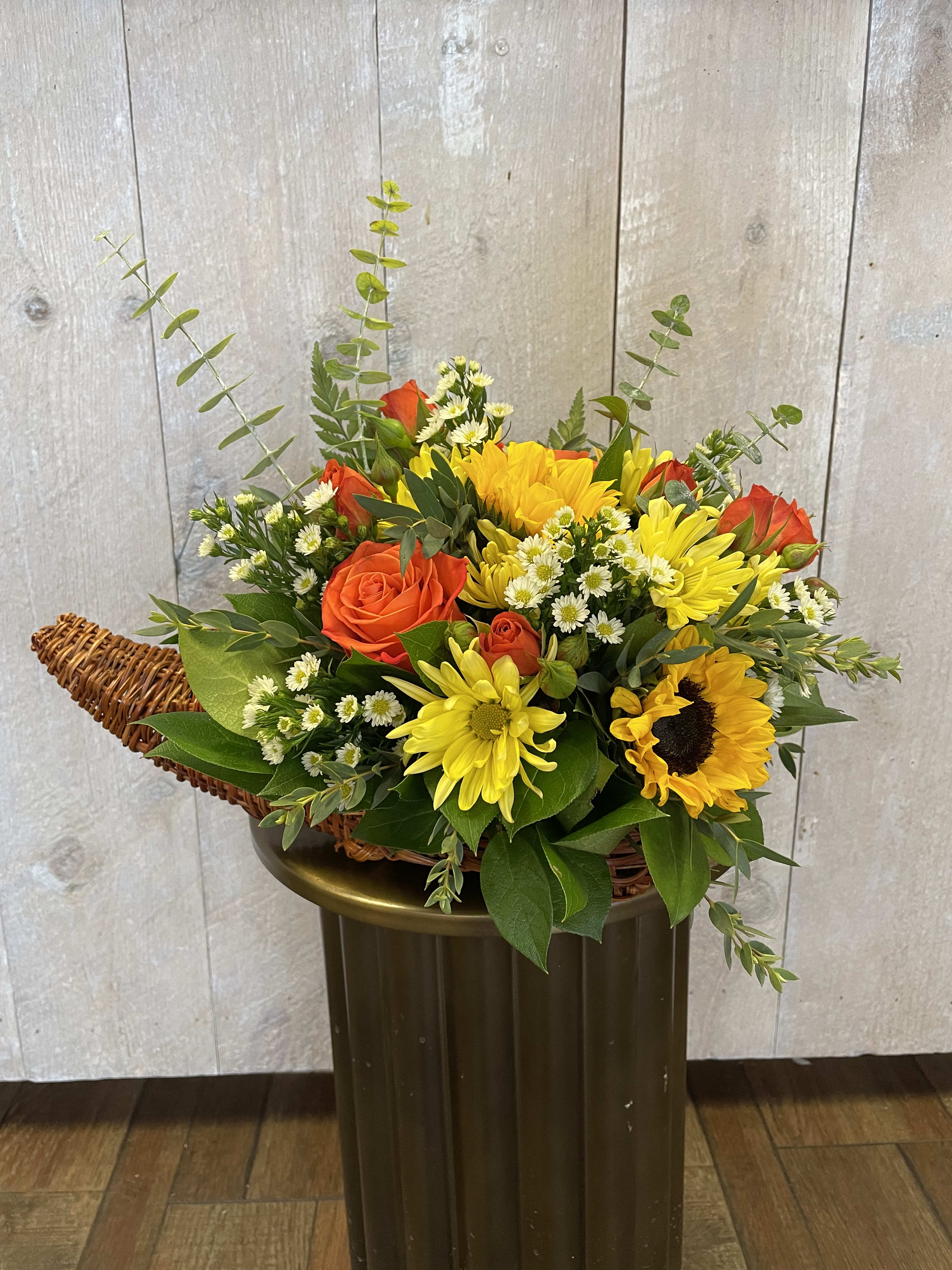 Bountiful Harvest Cornucopia Centerpiece - Give thanks this Thanksgiving with the gift of flowers! This one-sided cornucopia arrangement features fall-inspired blooms such as sunflowers, orange roses, daisies and mixed greens. Perfect to send as a gift or to put on your Thanksgiving table!