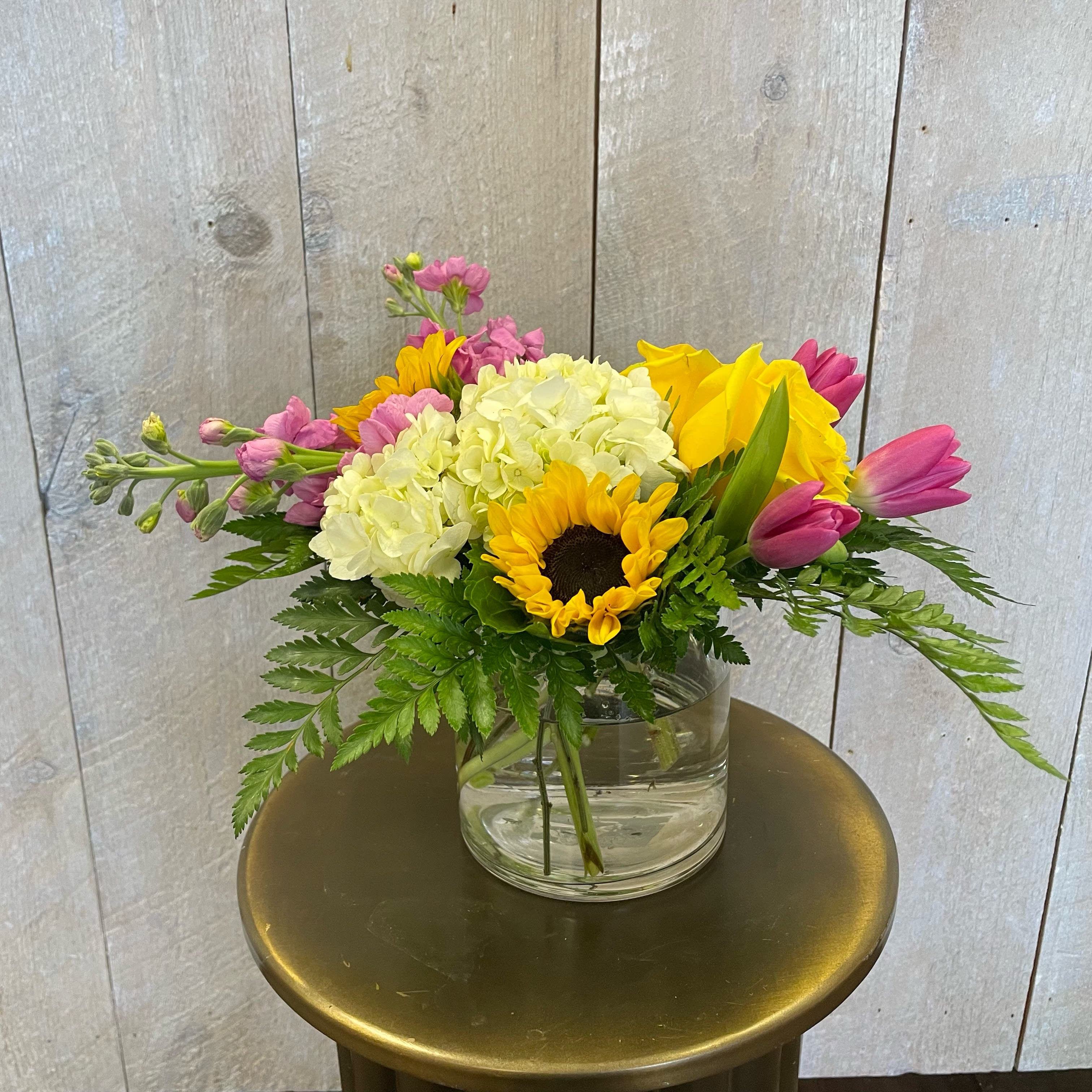 Mixed bouquet with sunflowers, hydrangeas, tulips, and pink stock in a glass vase