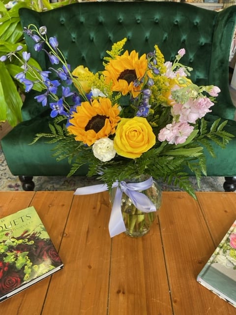 Bouquet of sunflowers, yellow roses, and blue flowers in a glass vase