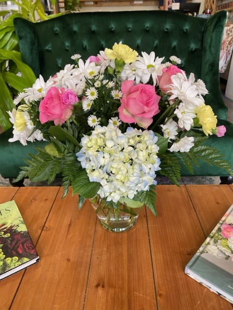 Pink roses and white daisies arranged in a glass vase with blue hydrangea