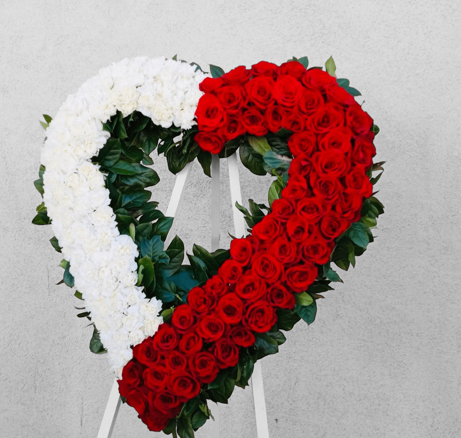 Blessed Heart - Make a strong, stylish statement of love with this beautiful heart-shaped wreath. Presented on a funeral easel, the rich red rose and white Carnation sympathy arrangement is a lovely standing spray to place on the altar or by the entrance to the service.
