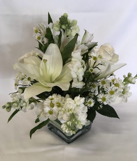 Compact white lily, rose, and daisy arrangement in a clear glass cube vase