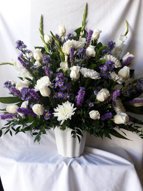 Tall white and purple flower arrangement with roses and mums in a white pot