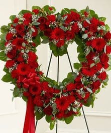 Heart-shaped wreath of red flowers with a red ribbon on a stand