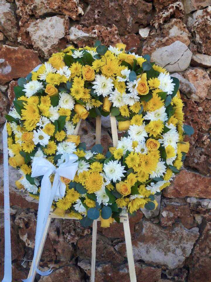 Yellow and white floral wreath on a stand with a white ribbon