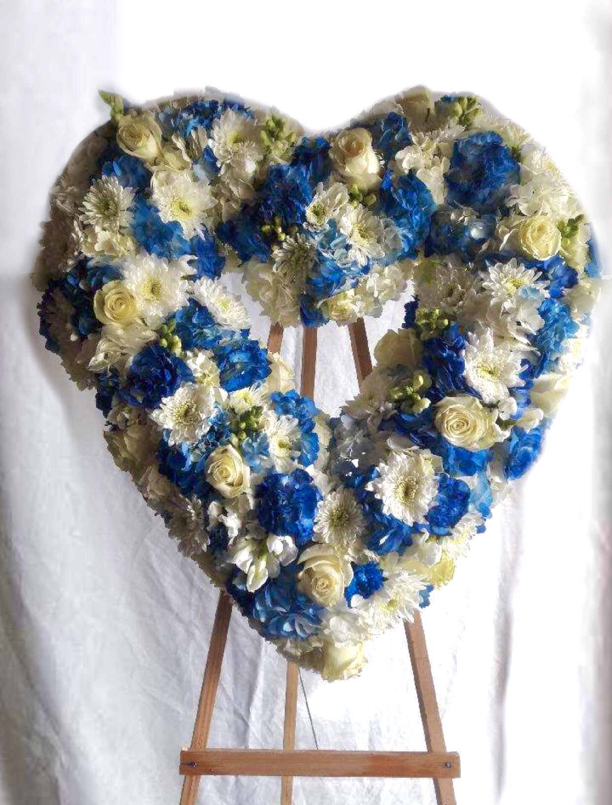 Heart-shaped floral arrangement on an easel with blue and white flowers