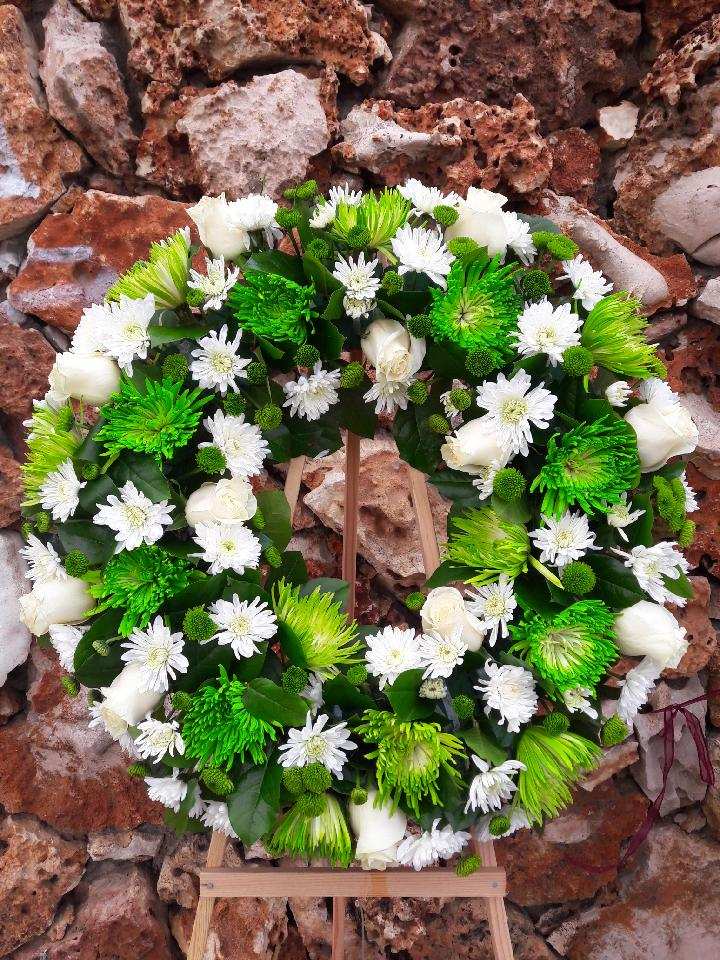 Circular floral wreath with white and green flowers on a wooden stand