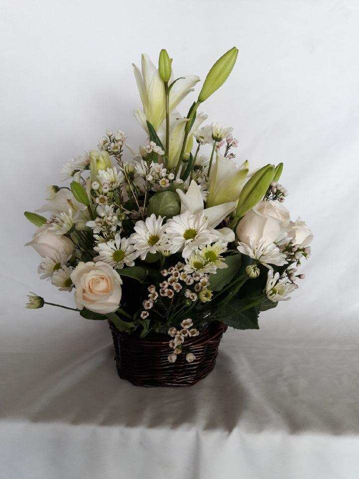 White lilies and roses arranged in a dark woven basket