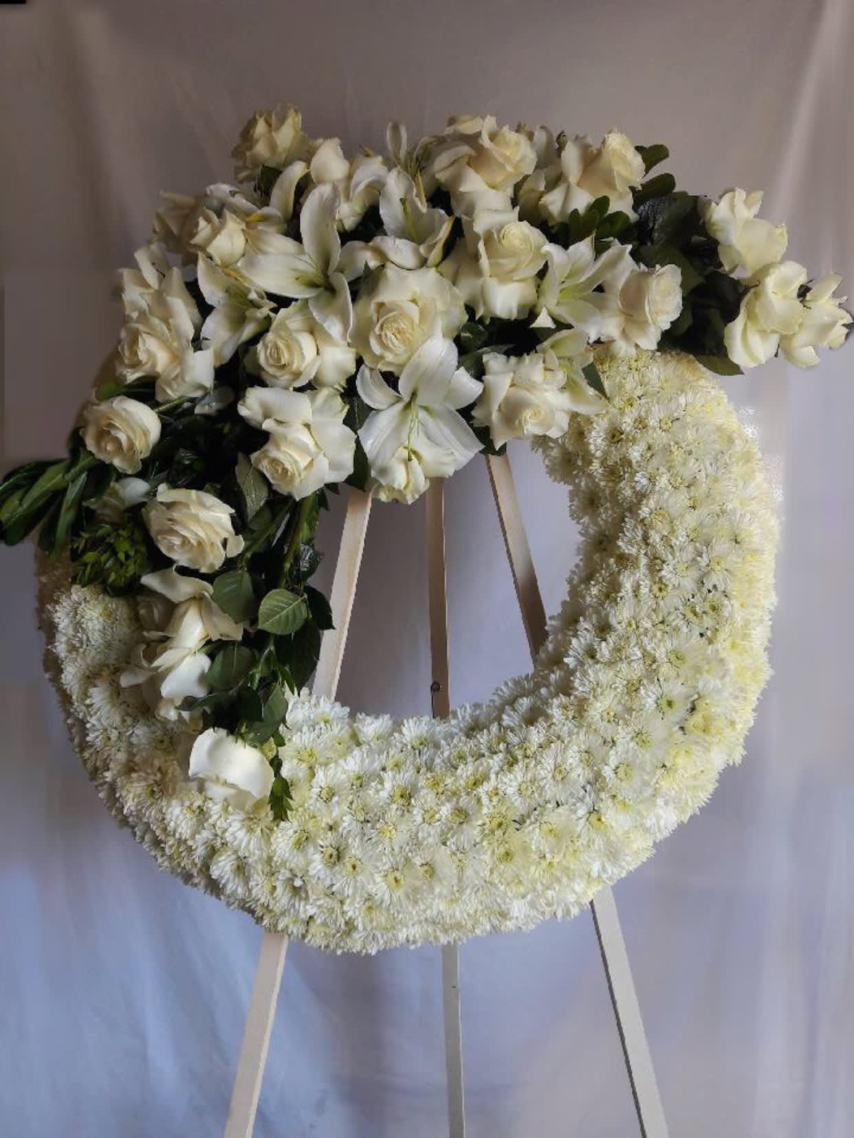 White floral funeral wreath on a stand with roses and lilies