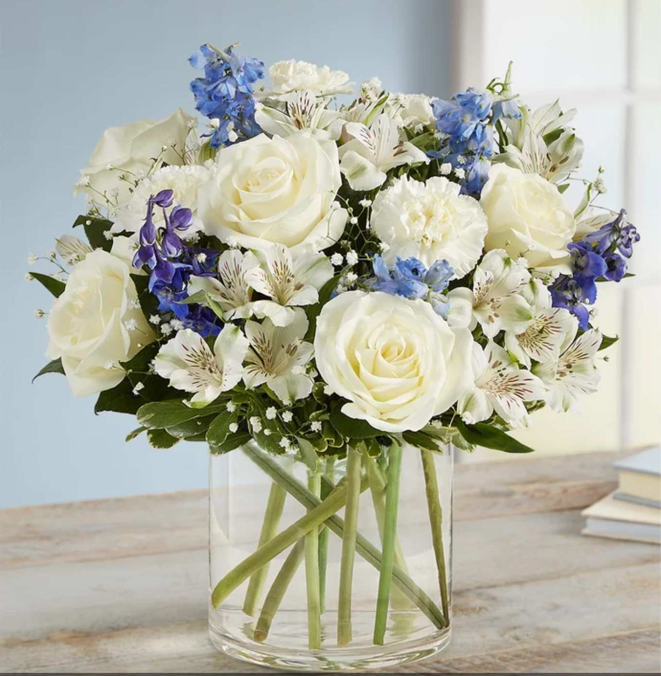 White roses and blue flowers arranged in a clear glass vase