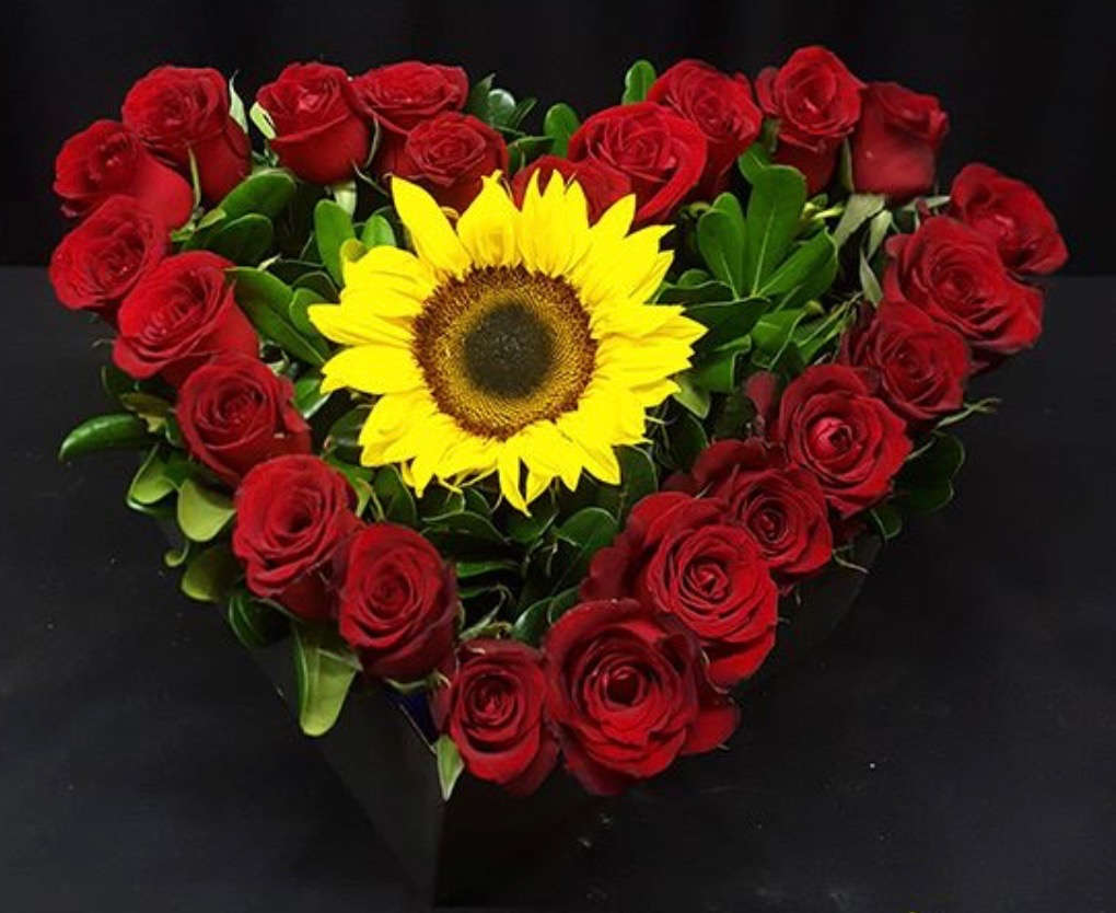 Heart-shaped bouquet of red roses with a yellow sunflower center
