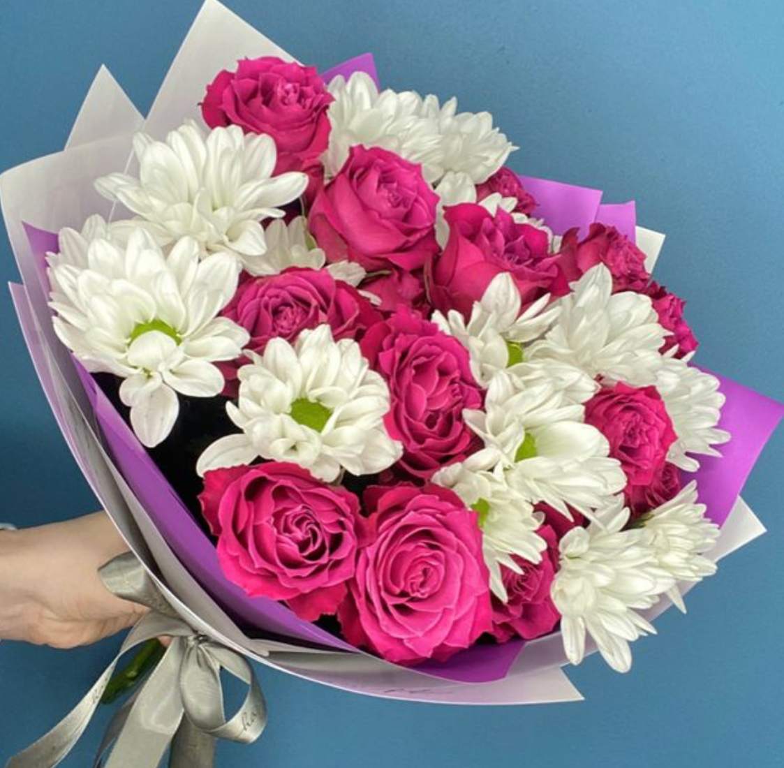 Bouquet of pink roses and white daisies wrapped in purple paper