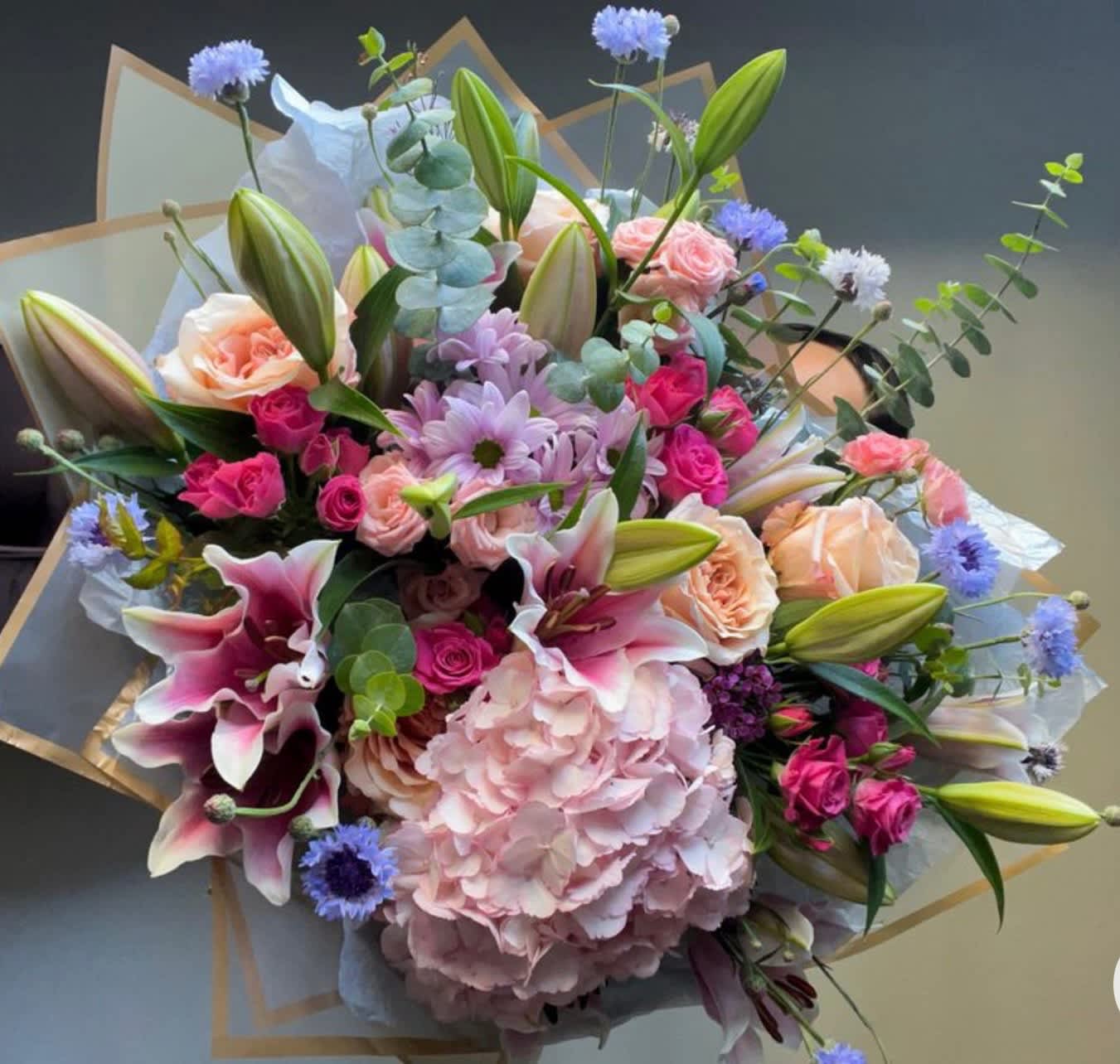 Mixed bouquet with pink lilies, roses, hydrangea, and blue accent flowers