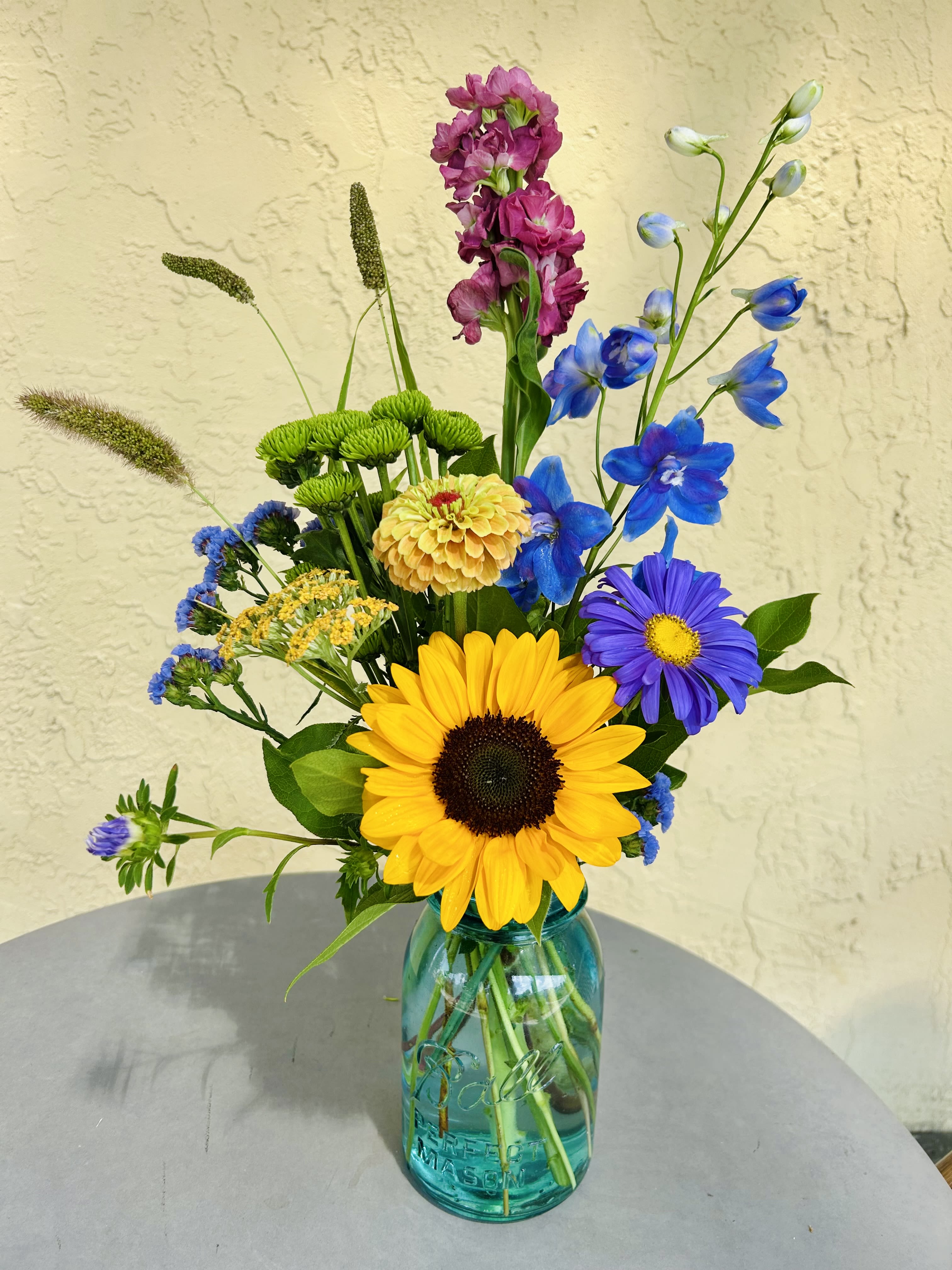 Mixed bouquet in a blue glass mason jar with a sunflower and blue flowers