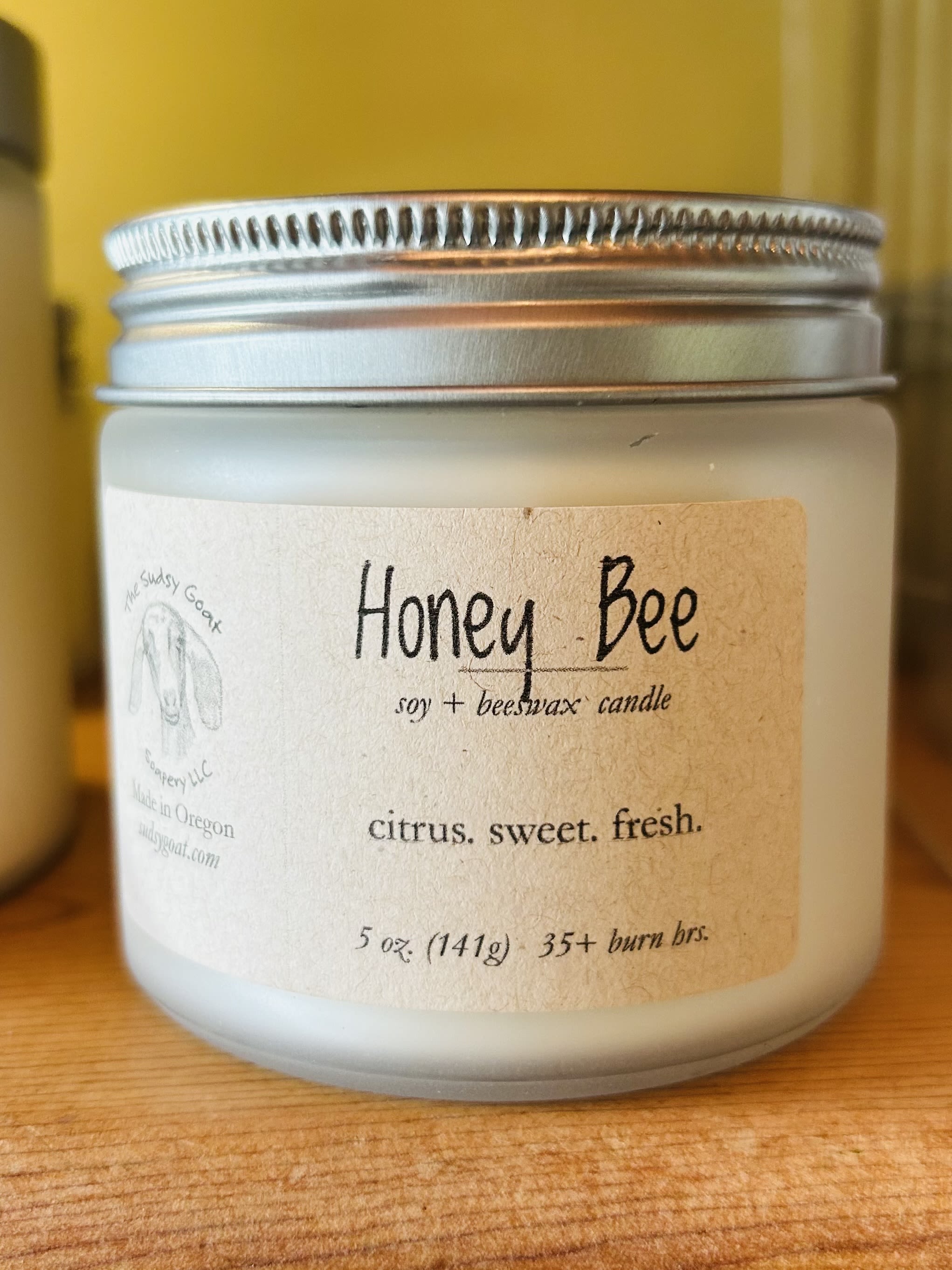 A frosted jar candle with a silver lid and Honey Bee label