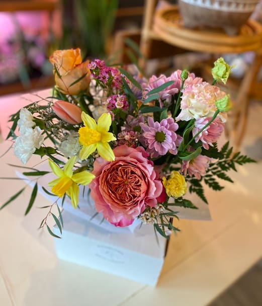 Mixed bouquet of pink, yellow, and white flowers in a white box