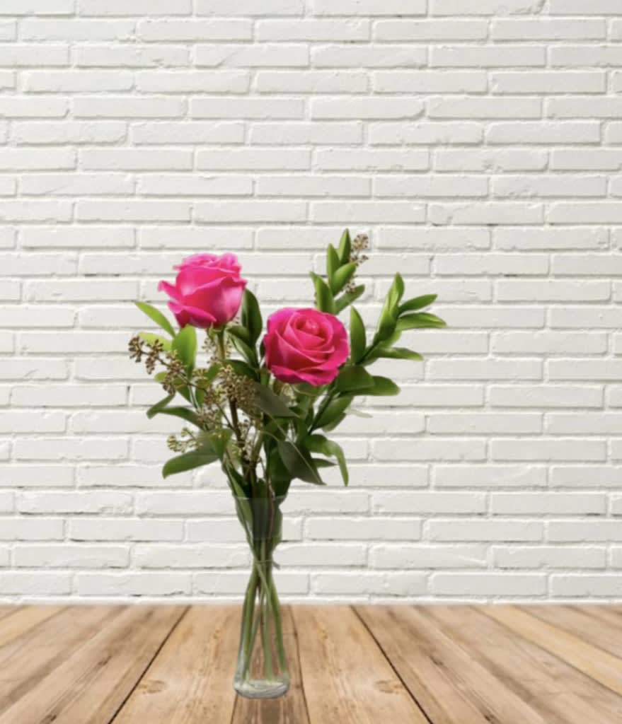 Two pink roses in a clear glass vase with greenery