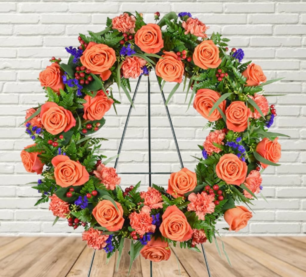 Circular floral wreath with orange roses and pink carnations on a stand