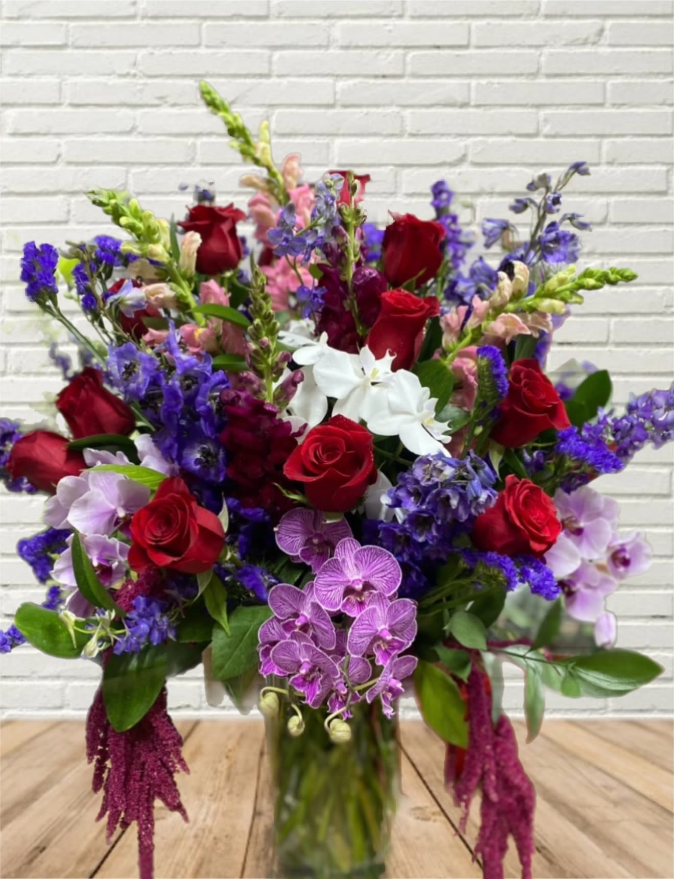 Bouquet of red roses, purple orchids, and white flowers in a glass vase