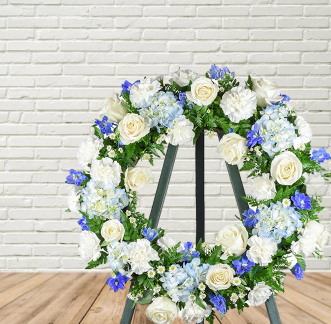 Floral wreath with white roses, blue hydrangeas, and white blooms on an easel