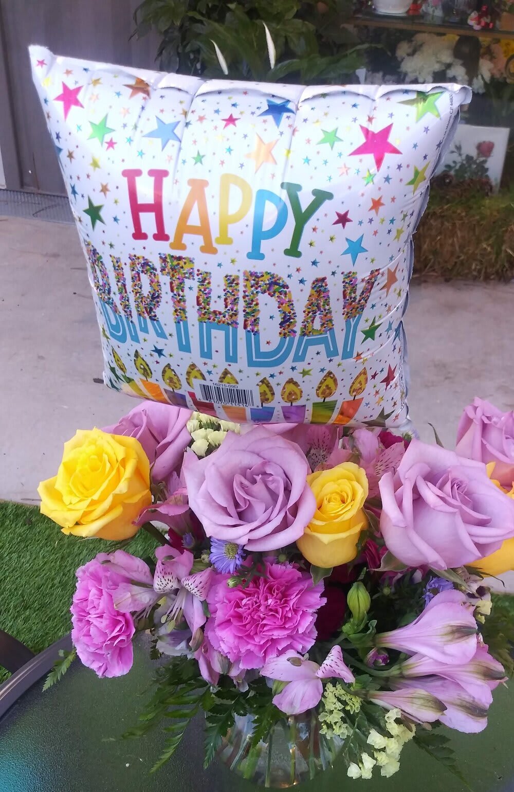 Birthday balloon above a bouquet of roses and pink flowers in a glass vase