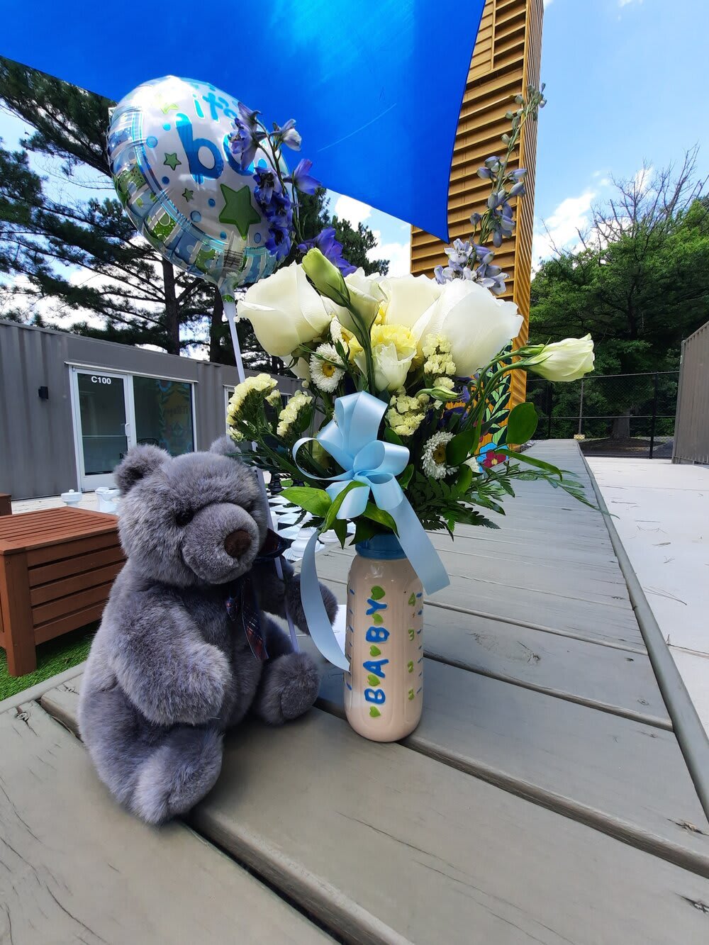 Bouquet of white and pale yellow flowers in a decorated bottle with a teddy bear and baby balloon