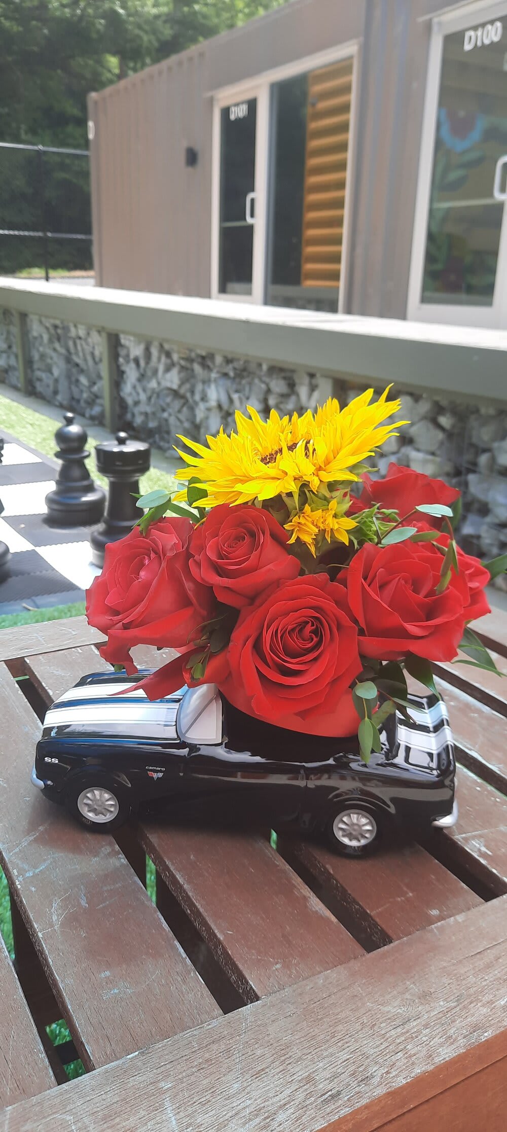 Red roses and yellow sunflowers arranged in a black truck-shaped vase