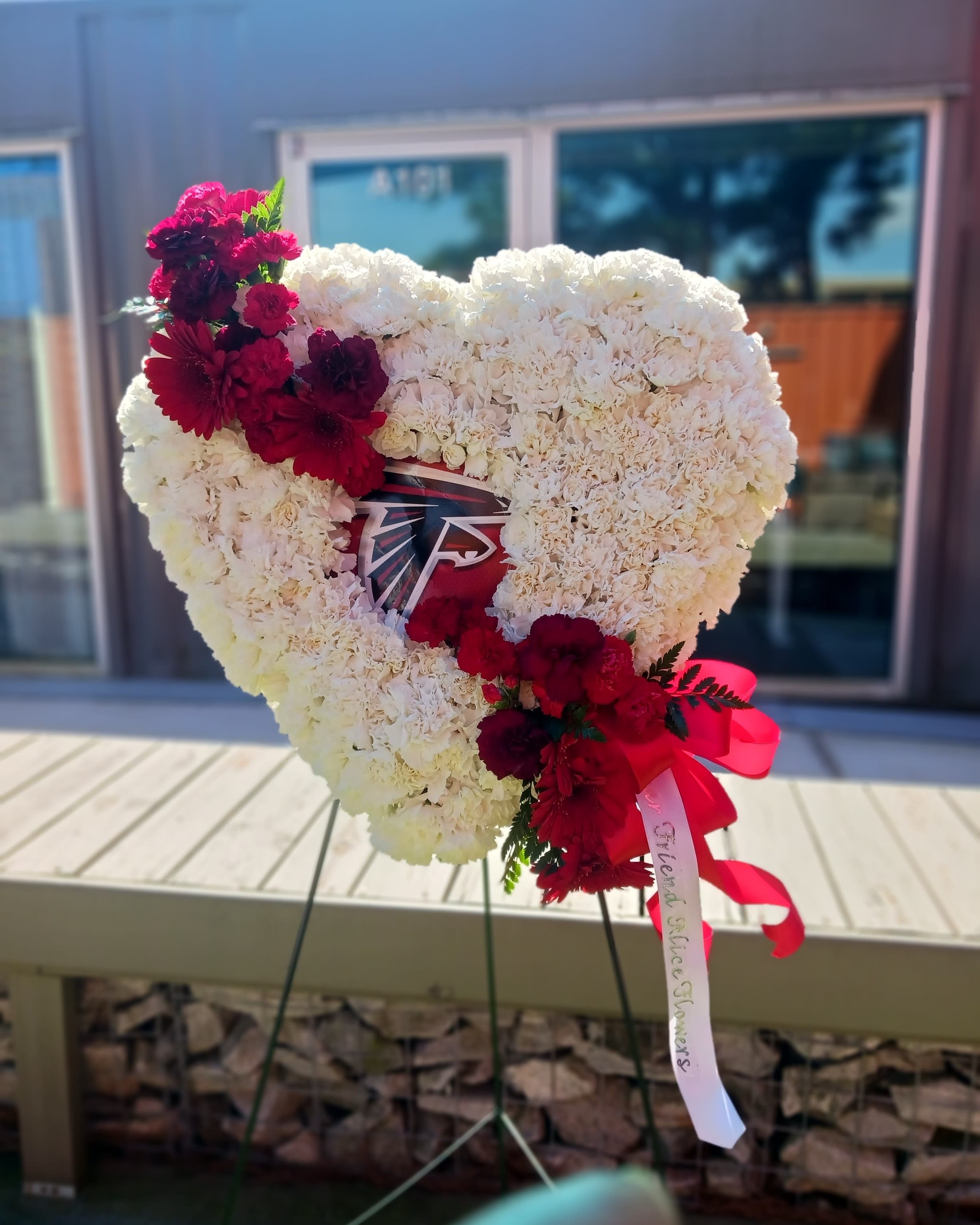 Heart-shaped white floral tribute with red flowers and ribbon