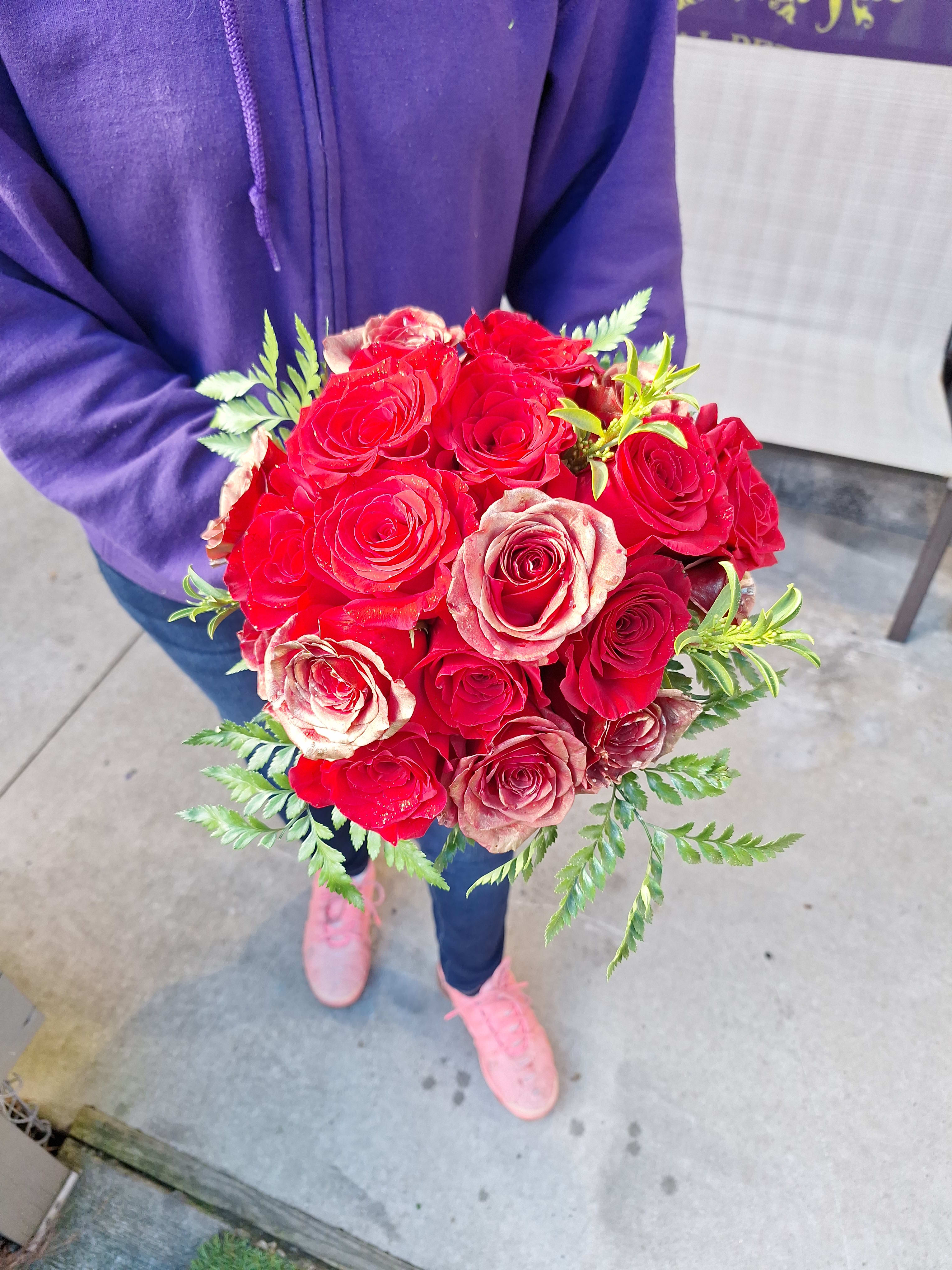 Handheld bouquet of red and blush roses with fern accents