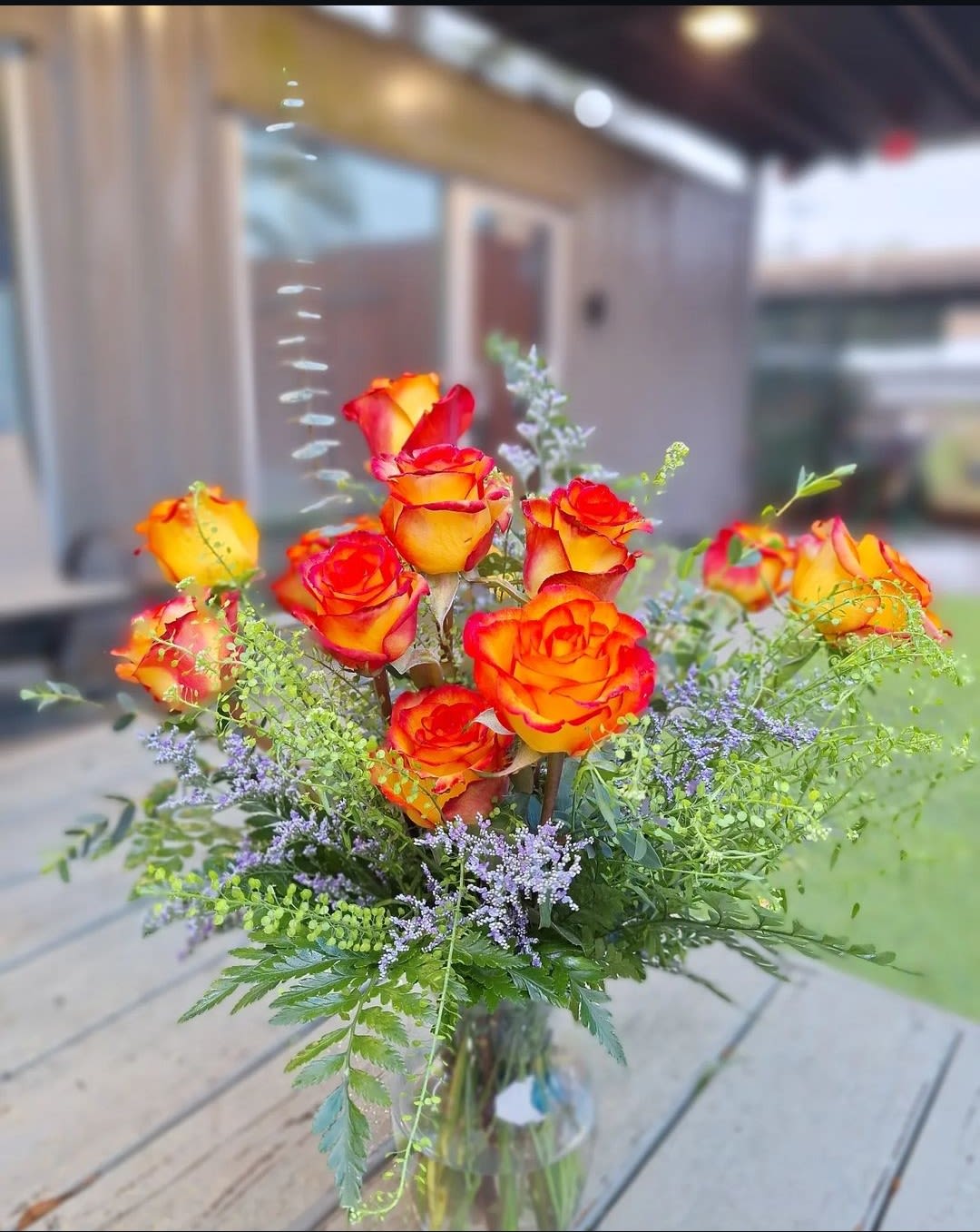 Orange and red roses in a glass vase with purple filler flowers