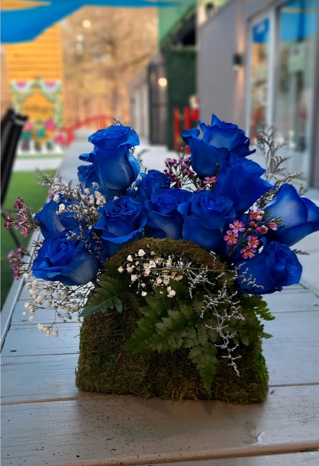 Blue roses arranged in a moss-covered box with small filler flowers