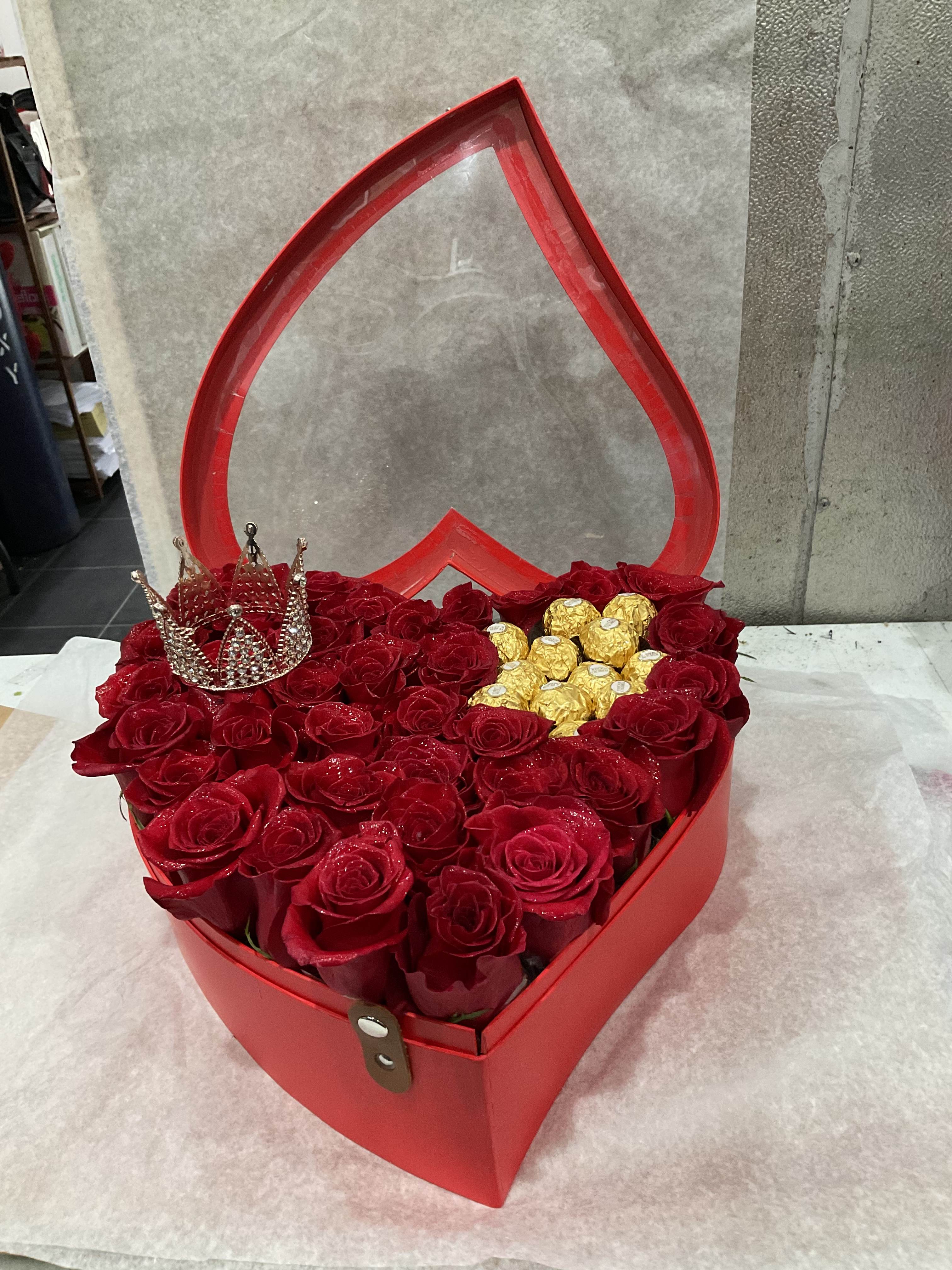 Red roses arranged in a heart-shaped gift box with gold chocolates and a jeweled crown