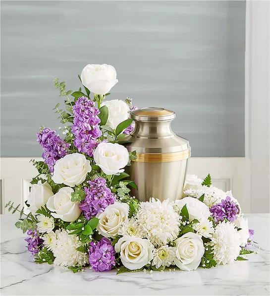 Cremation Wreath- Lavender &amp; White - Honor their memory and celebrate the joy they brought to their loved ones. Our wreath arrangement is handcrafted from peaceful white blooms, creating a beautiful tribute, while offering comfort during a difficult time.All-around asymmetrical wreath arrangement Lavender &amp; White roses, football mums, cushion poms and stock; accented with baby’s breath and assorted greenery .Urn Not Included