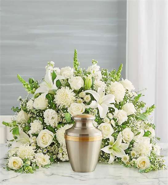 Crescent Cremation Arrangement- All White - Express your heartfelt condolences with a beautiful floral tribute.One-sided arrangement of white roses, Oriental lilies, snapdragon, football mums, button poms, carnations, stock, waxflower and monte casino; accented with baby’s breath and assorted greenery ( Urn &amp; Picture Frame Not Included )