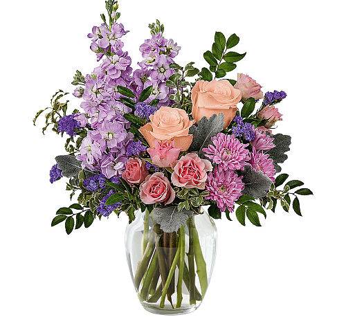 Pastel Perfection - Introducing "Pastel Perfection," a stunning floral arrangement capturing the delicate beauty of spring. It features soft pink spray roses, lavender stock, pink mums, and purple statice to create an elegant and serene ambiance. Enhanced by lush greens, this arrangement radiates freshness and charm. Perfect for any space, it brings joy and tranquillity, evoking the essence of the season in a delightful display.