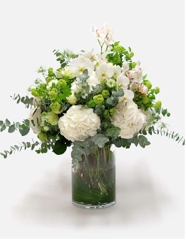 White orchids and hydrangeas in a glass vase with green accents