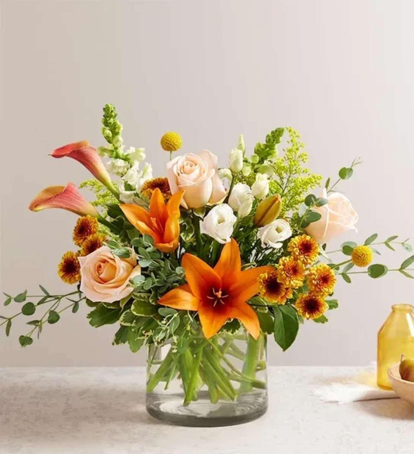 Autumn Amazement Bouquet  - Our nature-inspired bouquet captures all the amazement of autumn. Highlighted by unique, textural yellow craspedia, with rich tones of orange, peach, bronze and white, this loosely gathered arrangement arrives in a cylinder vase to brighten every gathering with beauty and charm