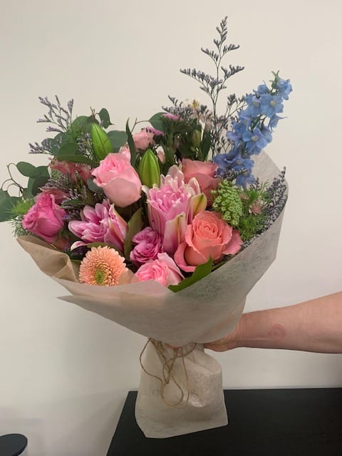 Hand-tied bouquet of pink and blue flowers wrapped in paper